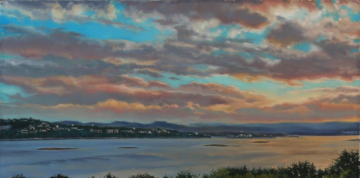 Wide coastal landscape beneath layered gray, pink, and gold clouds, with turquoise sky, calm water, distant hills, and small islands.