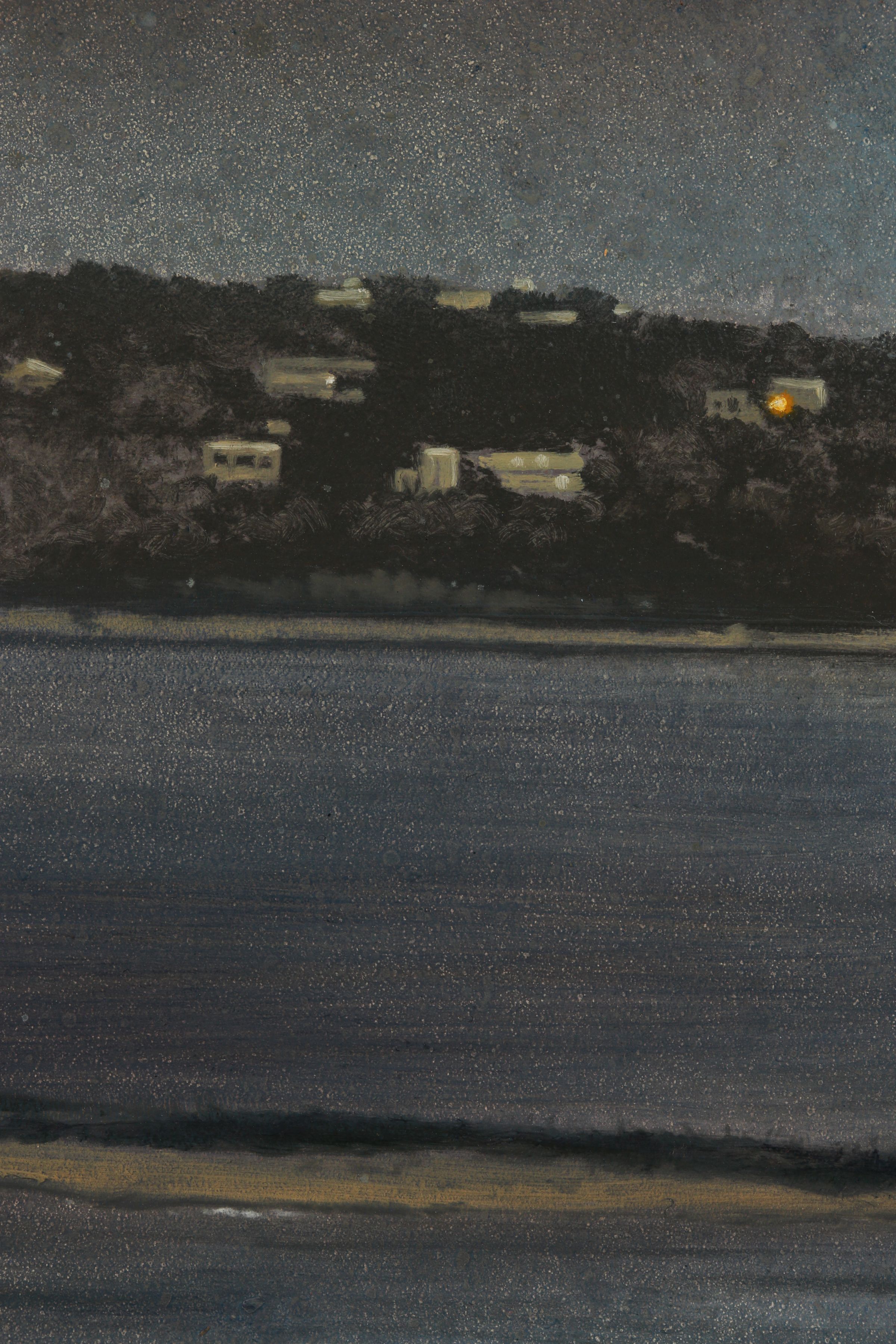 Close detail of a dark blue-gray lake beneath a wooded shoreline with scattered pale buildings and a single glowing orange light.