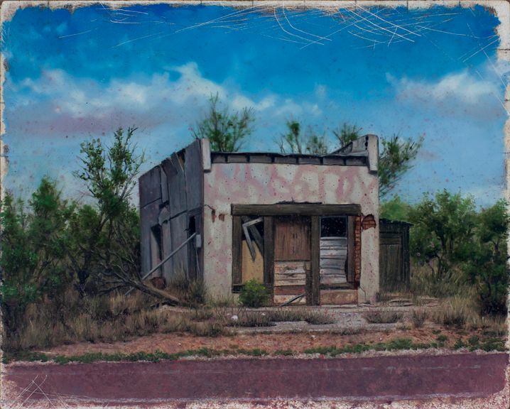 Small weathered building with boarded openings stands amid scrubby vegetation beneath a vivid blue, cloud-streaked sky.