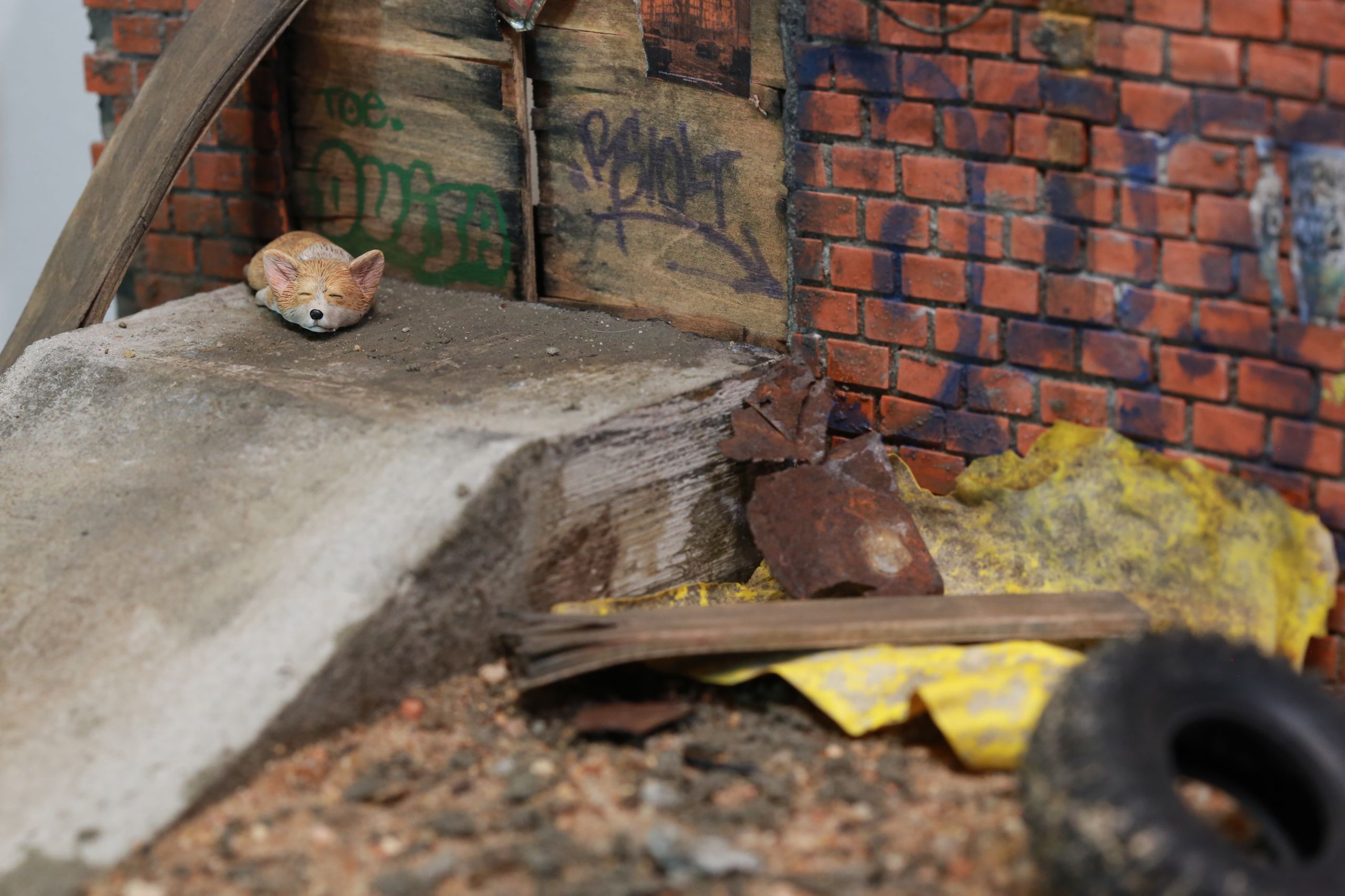 1/24-1/18 scale miniature diorama of a bombed out post apocalyptic inner city street alley way, with corrugated steel auto garage bay door, graffiti mural, and Frank Lloyd Wright Ennis House tiles