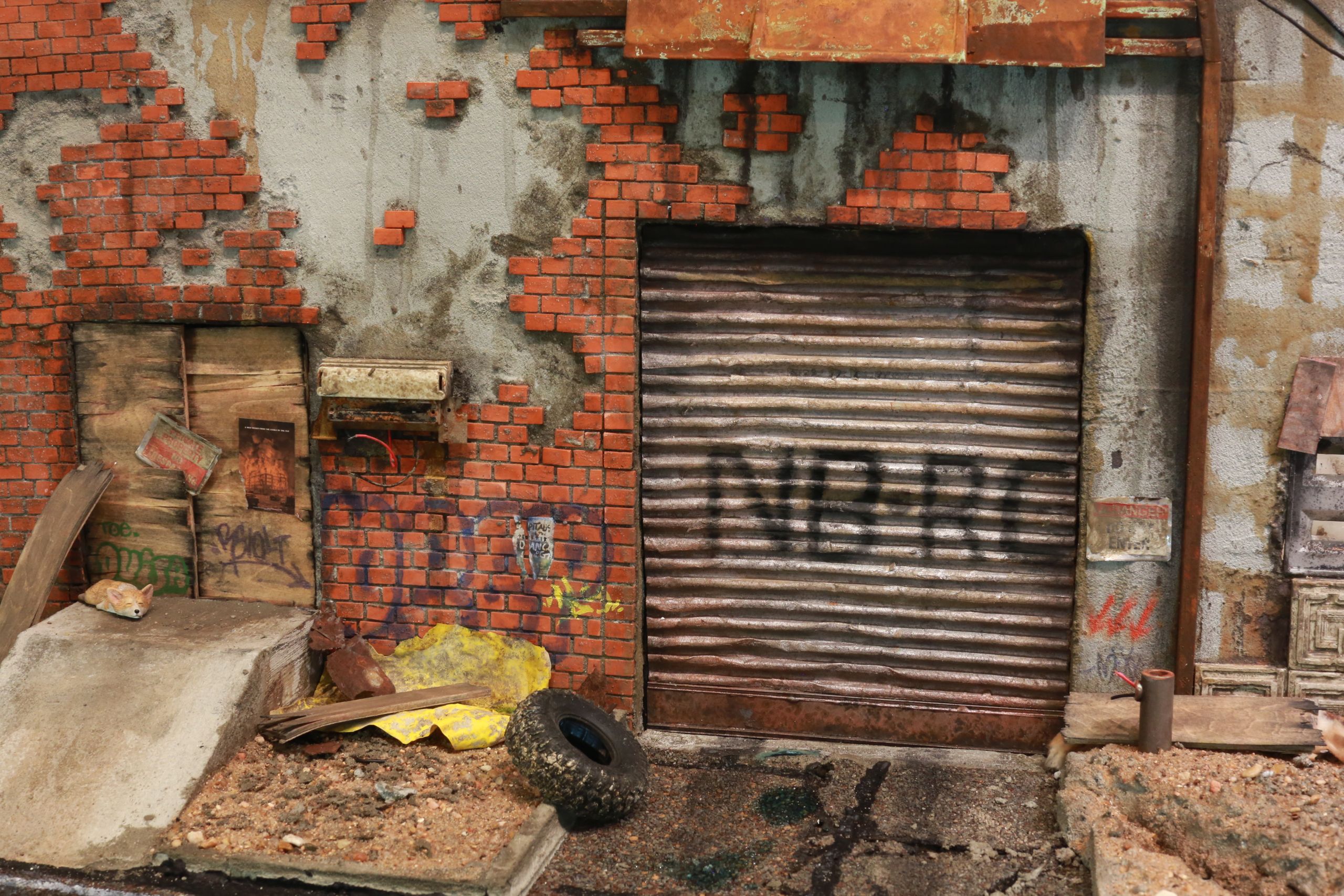 1/24-1/18 scale miniature diorama of a bombed out post apocalyptic inner city street alley way, with corrugated steel auto garage bay door, graffiti mural, and Frank Lloyd Wright Ennis House tiles