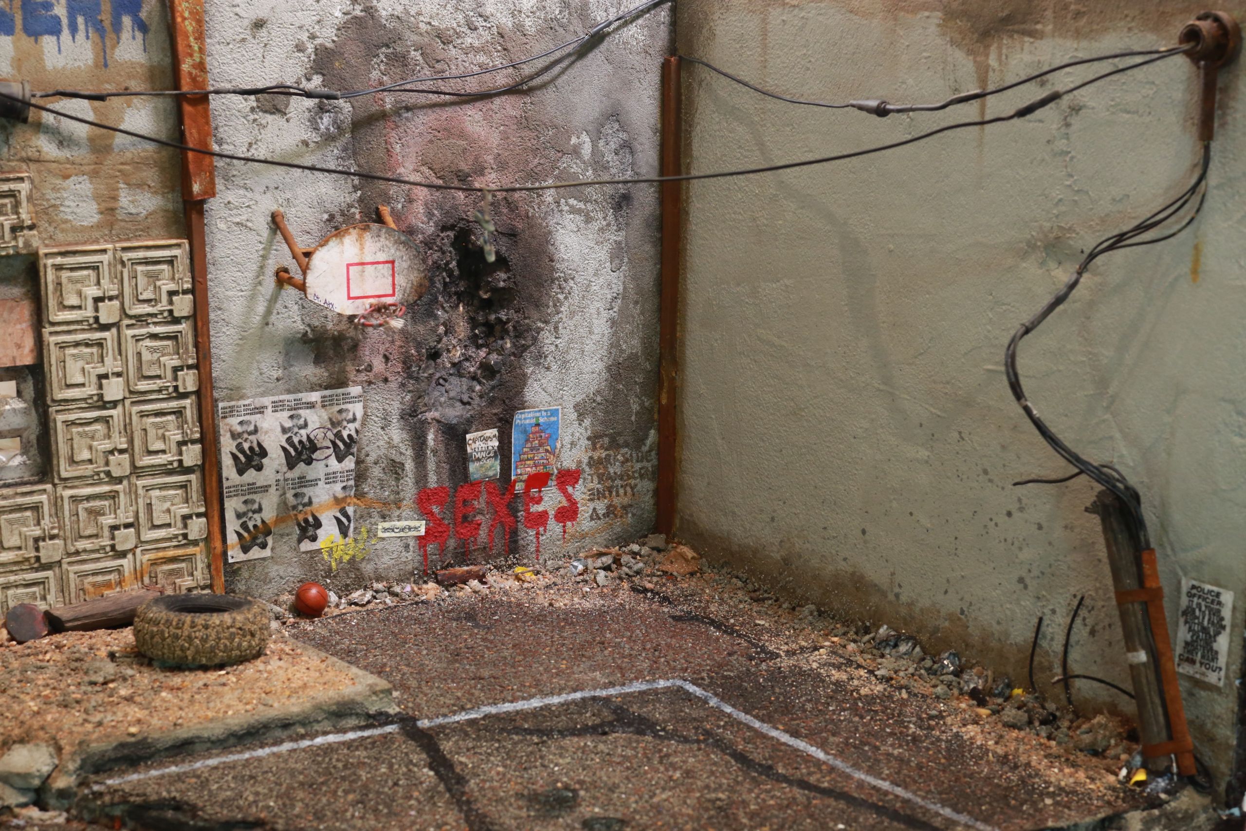 1/24-1/18 scale miniature diorama of a bombed out post apocalyptic inner city street alley way, with corrugated steel auto garage bay door, graffiti mural, and Frank Lloyd Wright Ennis House tiles