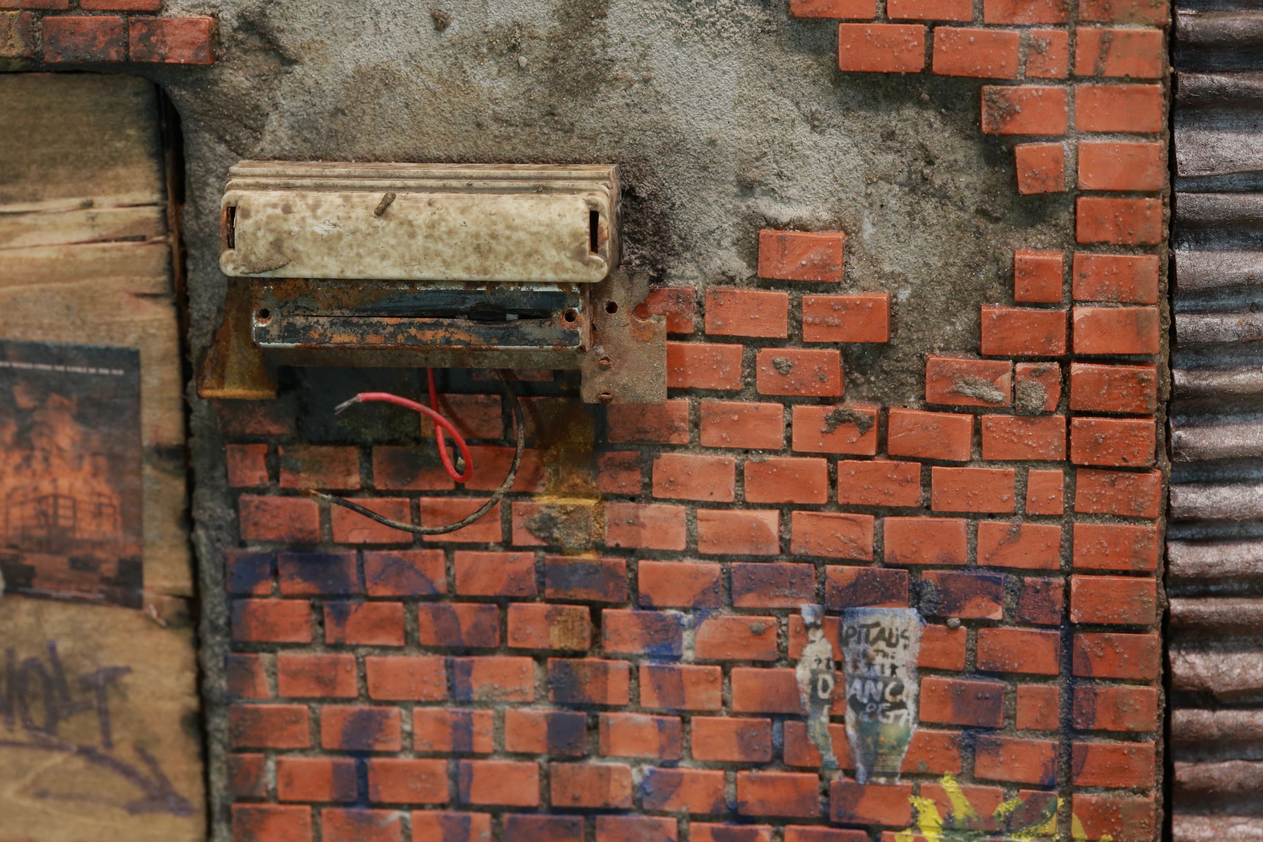 1/24-1/18 scale miniature diorama of a bombed out post apocalyptic inner city street alley way, with corrugated steel auto garage bay door, graffiti mural, and Frank Lloyd Wright Ennis House tiles