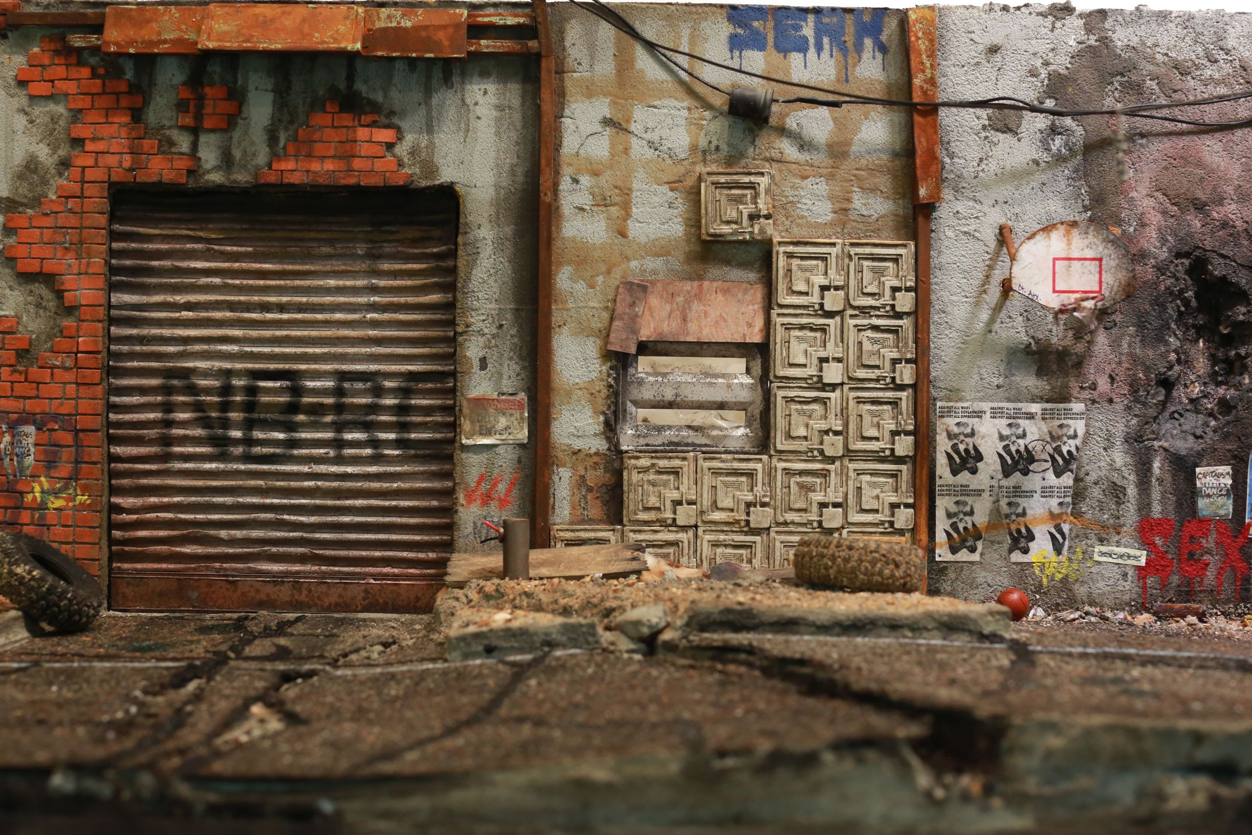 1/24-1/18 scale miniature diorama of a bombed out post apocalyptic inner city street alley way, with corrugated steel auto garage bay door, graffiti mural, and Frank Lloyd Wright Ennis House tiles