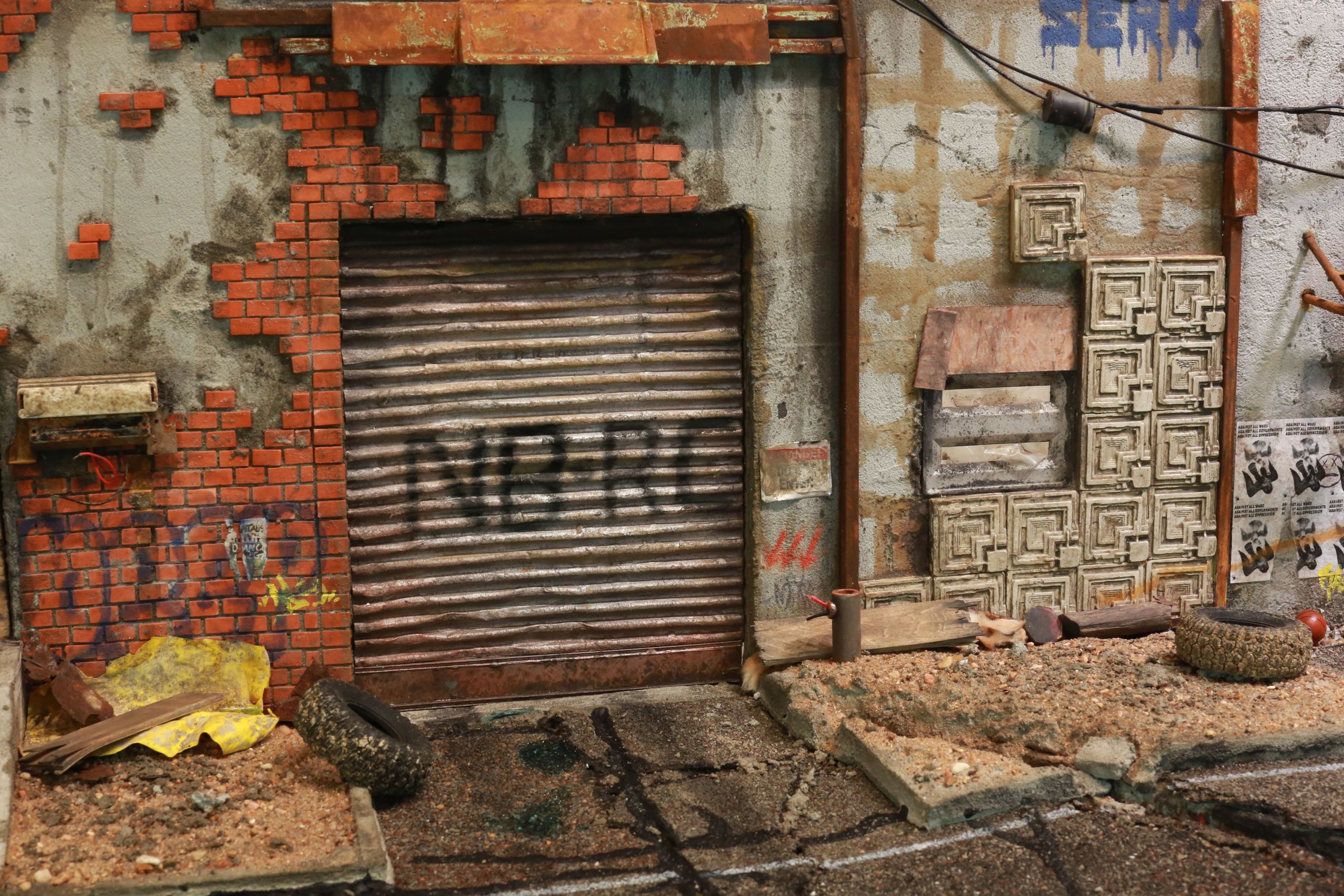 1/24-1/18 scale miniature diorama of a bombed out post apocalyptic inner city street alley way, with corrugated steel auto garage bay door, graffiti mural, and Frank Lloyd Wright Ennis House tiles