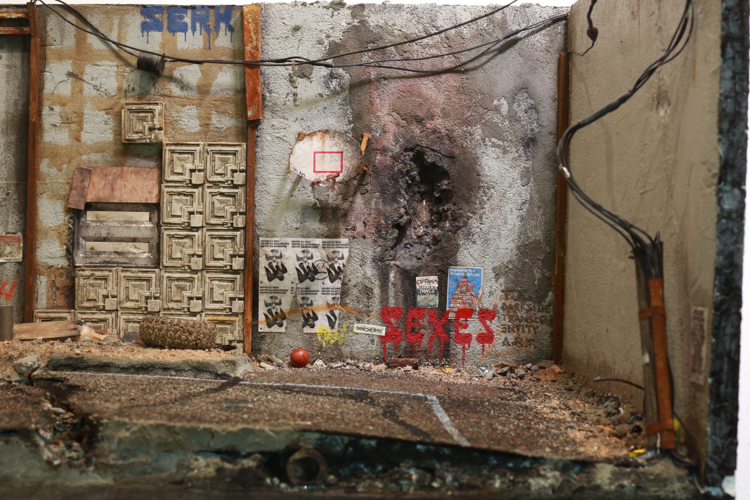 1/24-1/18 scale miniature diorama of a bombed out post apocalyptic inner city street alley way, with corrugated steel auto garage bay door, graffiti mural, and Frank Lloyd Wright Ennis House tiles
