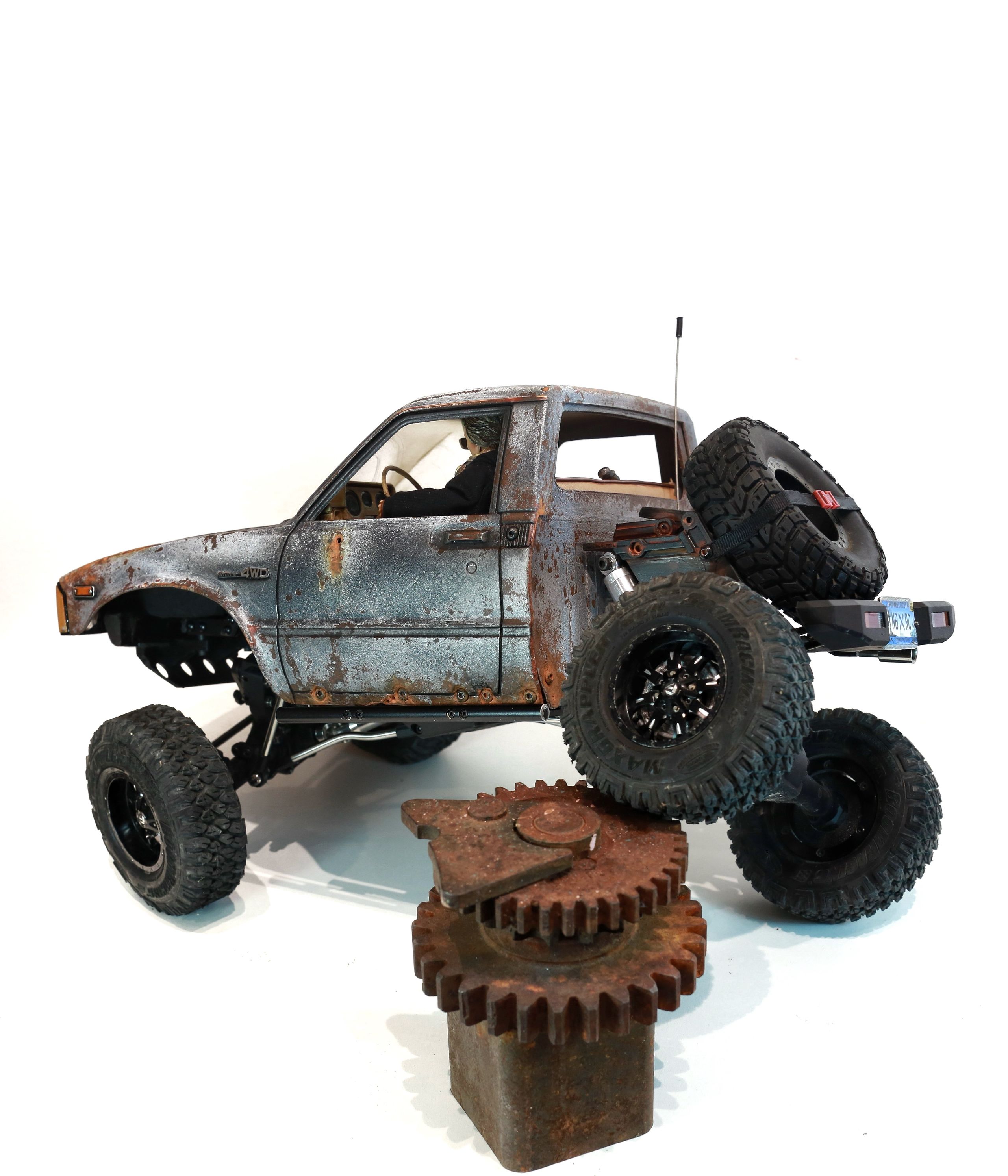 An old Toyota Hilux cab-only "beater" pickup truck working RC vehicle in 1/10 scale, with a gooseneck trailer hitch platform and carrying a spare wheel. Featuring a custom interior with action figure driver, handmade accessories, and faux leather bench seat.