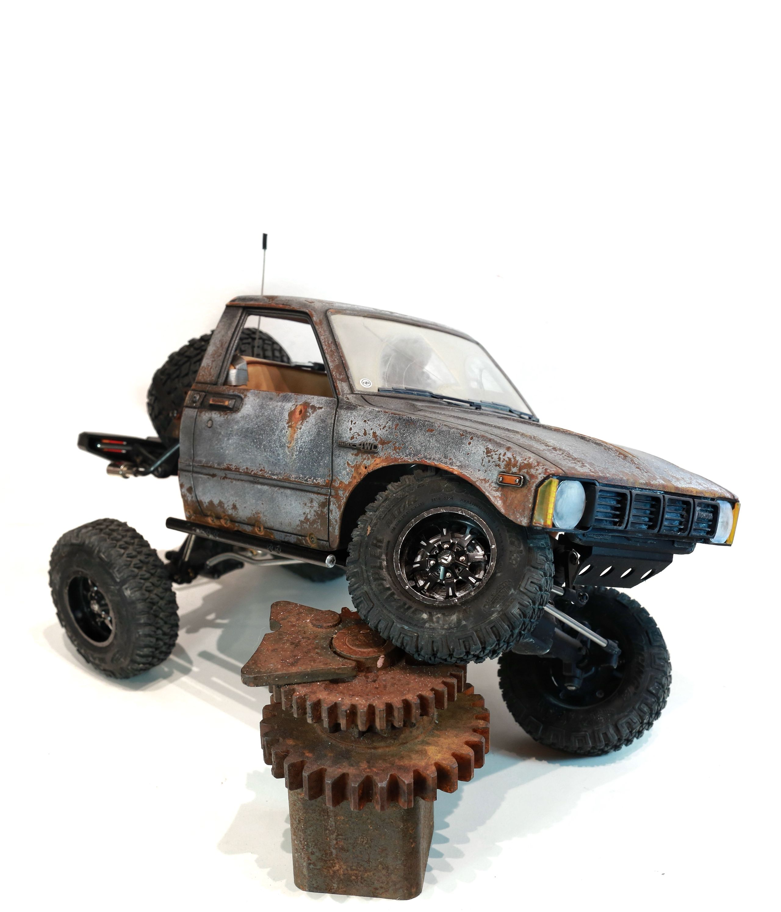 An old Toyota Hilux cab-only "beater" pickup truck working RC vehicle in 1/10 scale, with a gooseneck trailer hitch platform and carrying a spare wheel. Featuring a custom interior with action figure driver, handmade accessories, and faux leather bench seat.