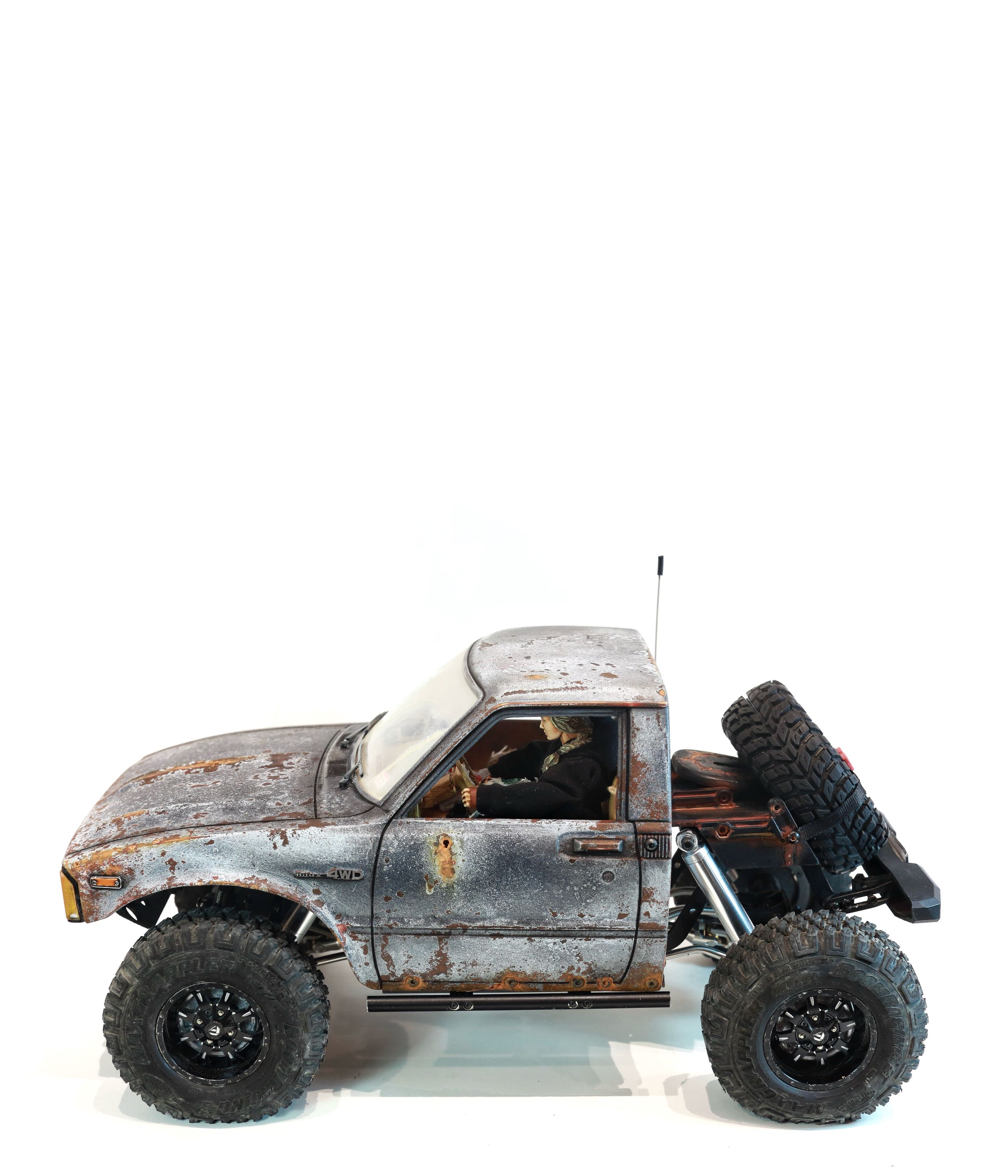 An old Toyota Hilux cab-only "beater" pickup truck working RC vehicle in 1/10 scale, with a gooseneck trailer hitch platform and carrying a spare wheel. Featuring a custom interior with action figure driver, handmade accessories, and faux leather bench seat.