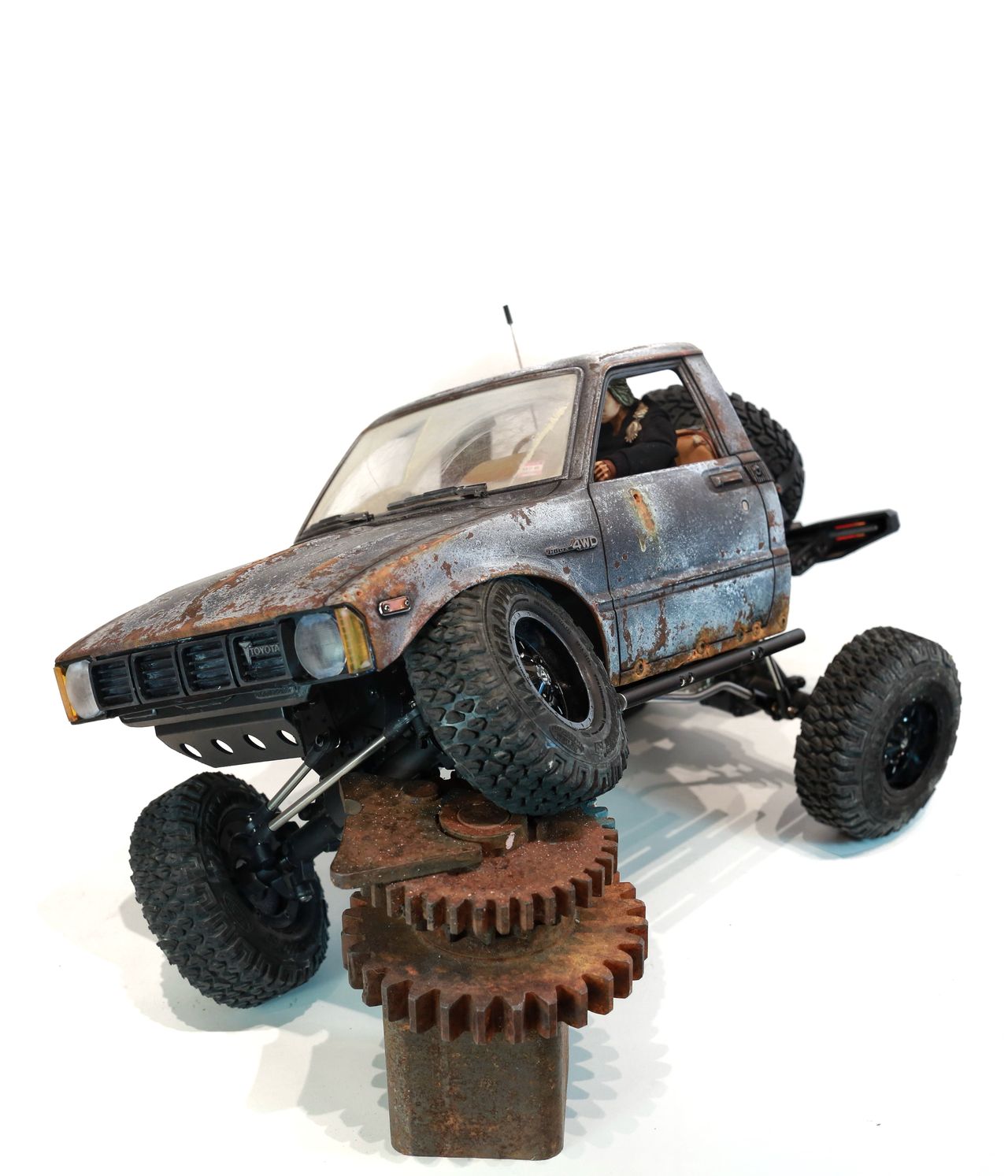 An old Toyota Hilux cab-only "beater" pickup truck working RC vehicle in 1/10 scale, with a gooseneck trailer hitch platform and carrying a spare wheel. Featuring a custom interior with action figure driver, handmade accessories, and faux leather bench seat.