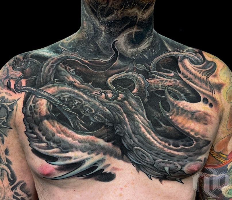 Close view of a chest bearing a medium-scale dark tattoo of twisting tentacles, skull-like forms, and a snarling creature.