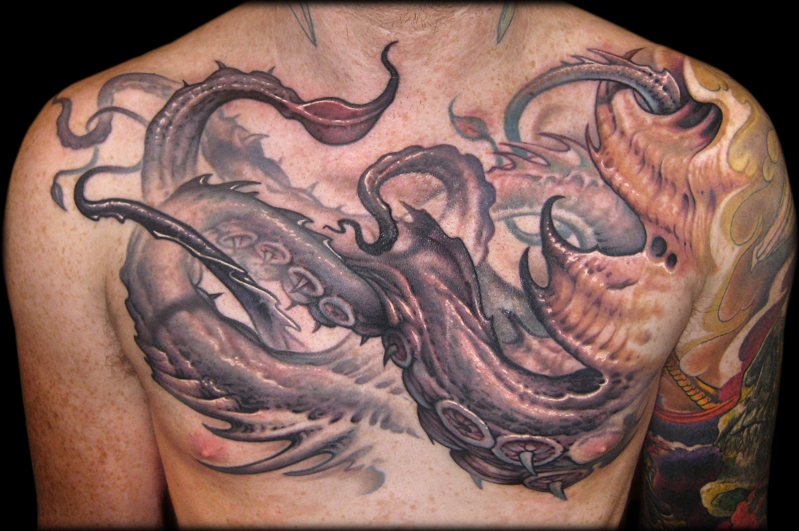 Close view of a chest tattoo showing a grey-purple tentacled creature spreading across the torso beside an orange skull.