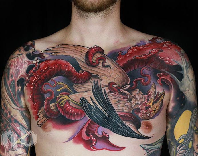 A medium chest tattoo depicts a winged bird entwined with a red serpentine creature in red, black, tan, and purple.