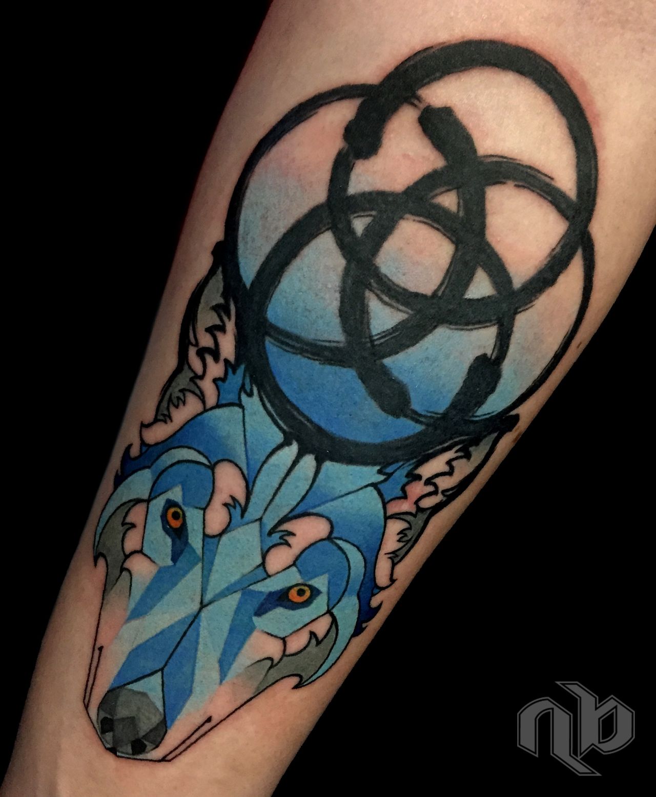 Close-up of an arm tattoo showing geometric faceted blue wolf head beneath bold, looping black circles forming a japanese enso symbol.