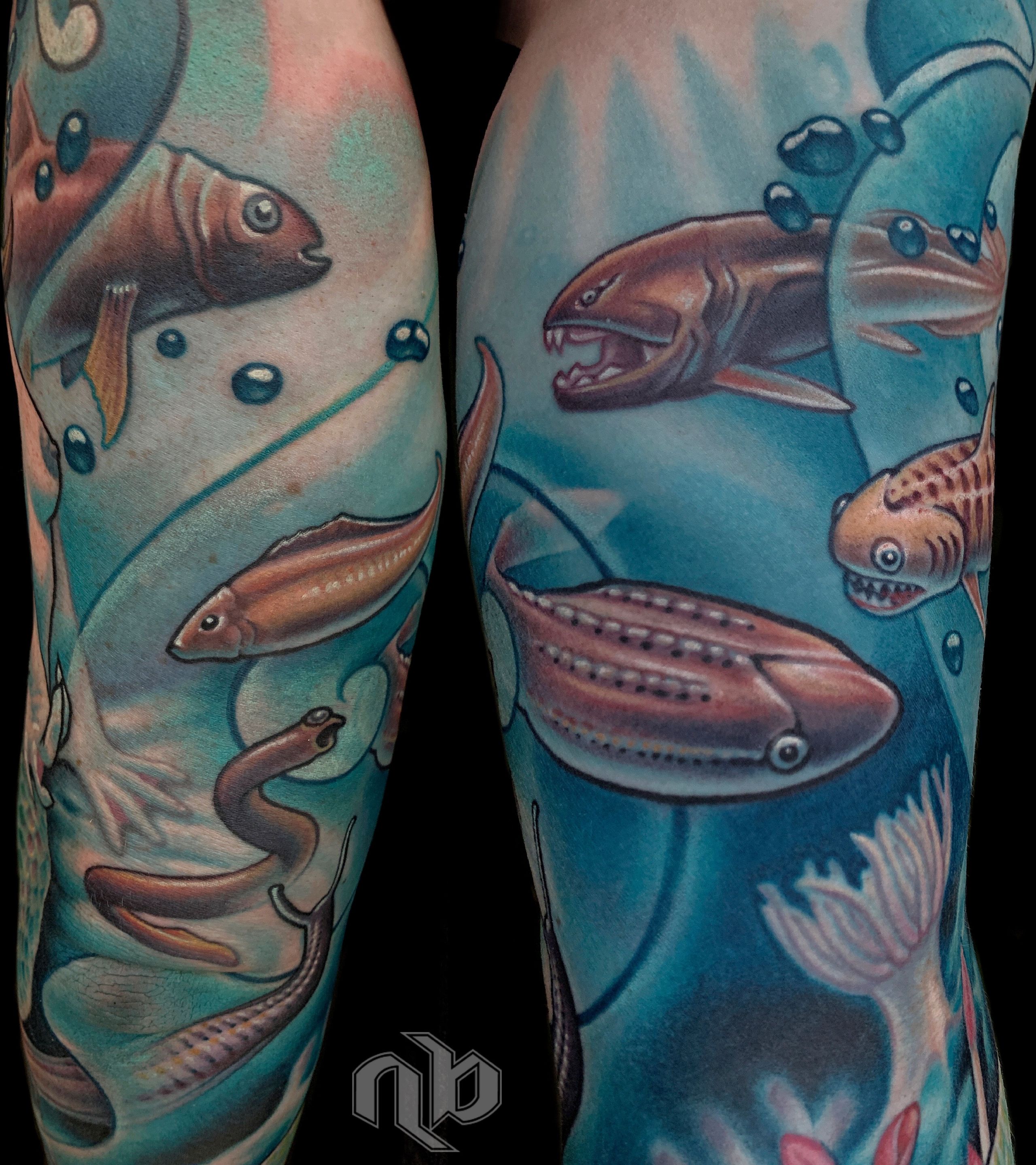 Close view of a large blue arm tattoo featuring prehistoric fish, sharks, eel-like creatures, bubbles, and aquatic plants.