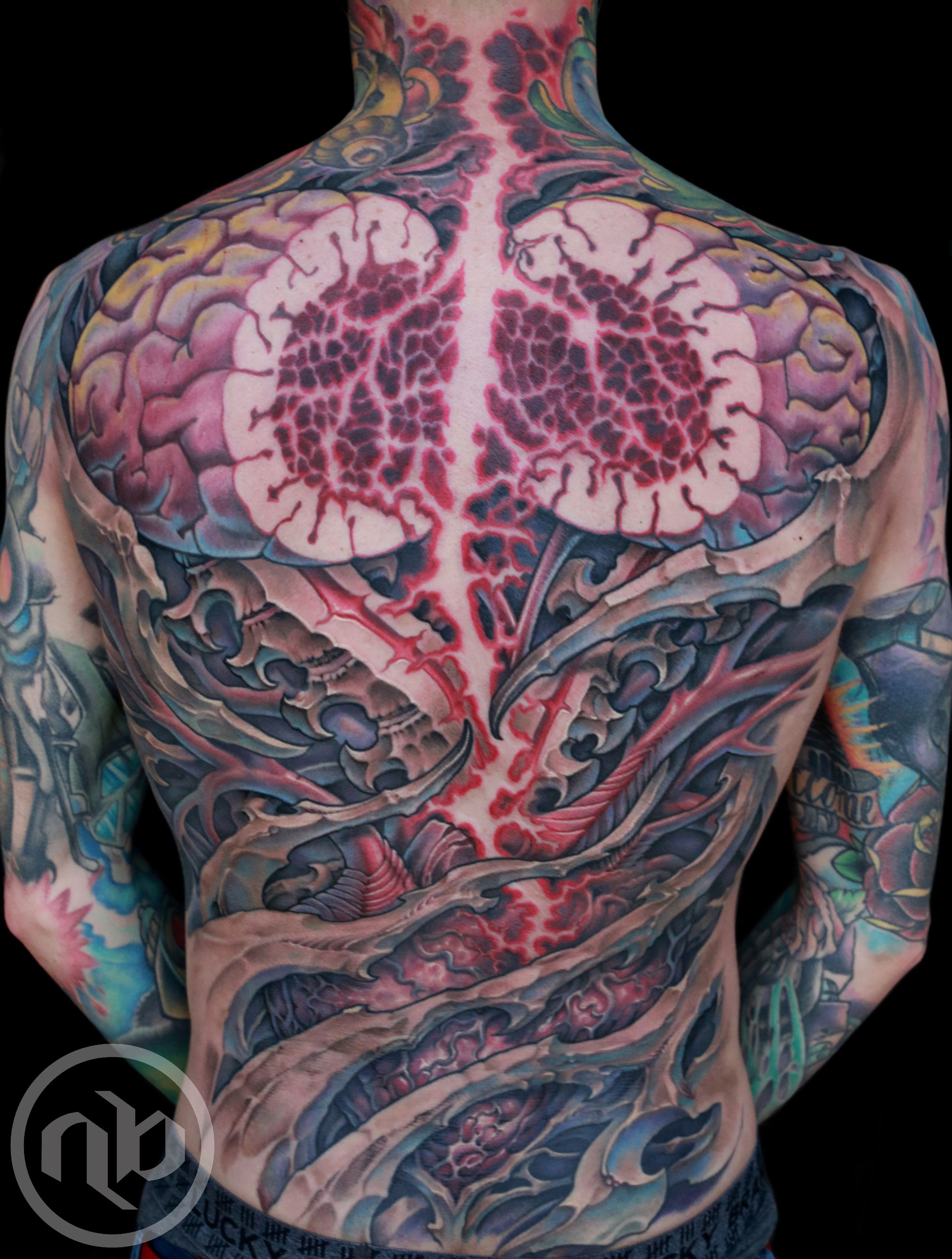 Wider rear view of a large back tattoo featuring split pink brain, a central red lightning pattern, a human heart, and layered blue-grey bio-organic forms.