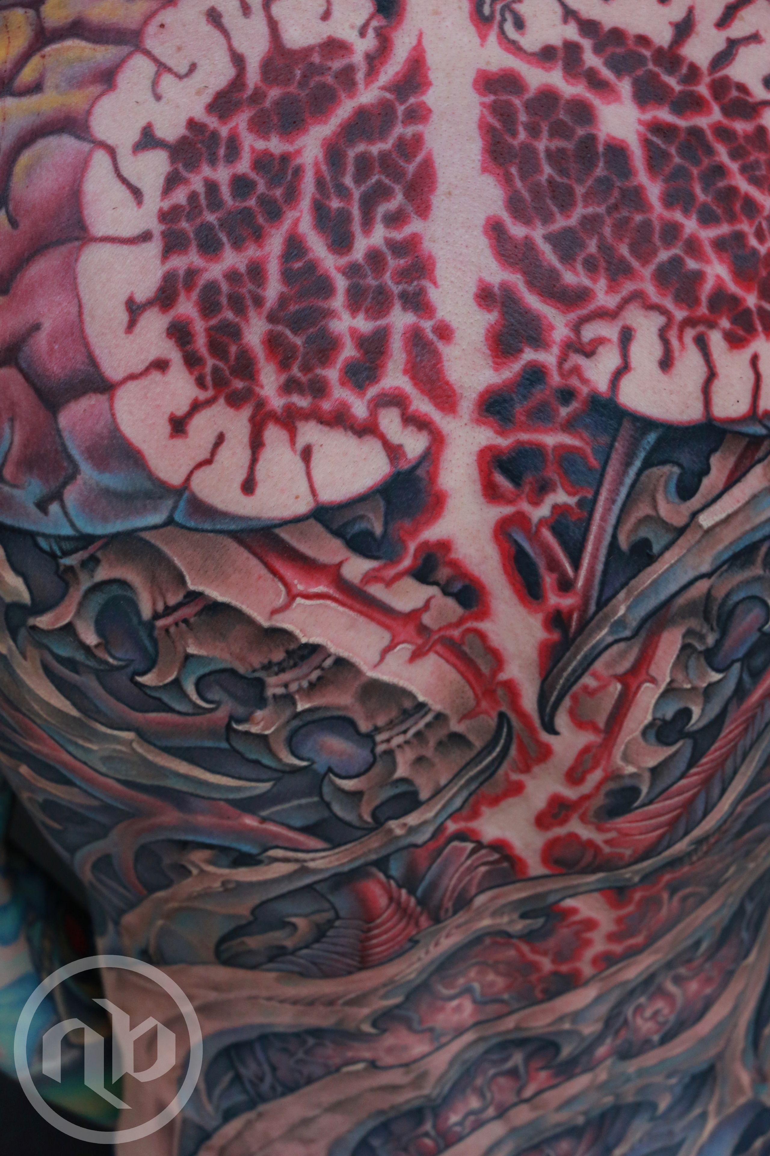 Close detail of a large back tattoo showing a split brain and bio-organic ornamental forms.