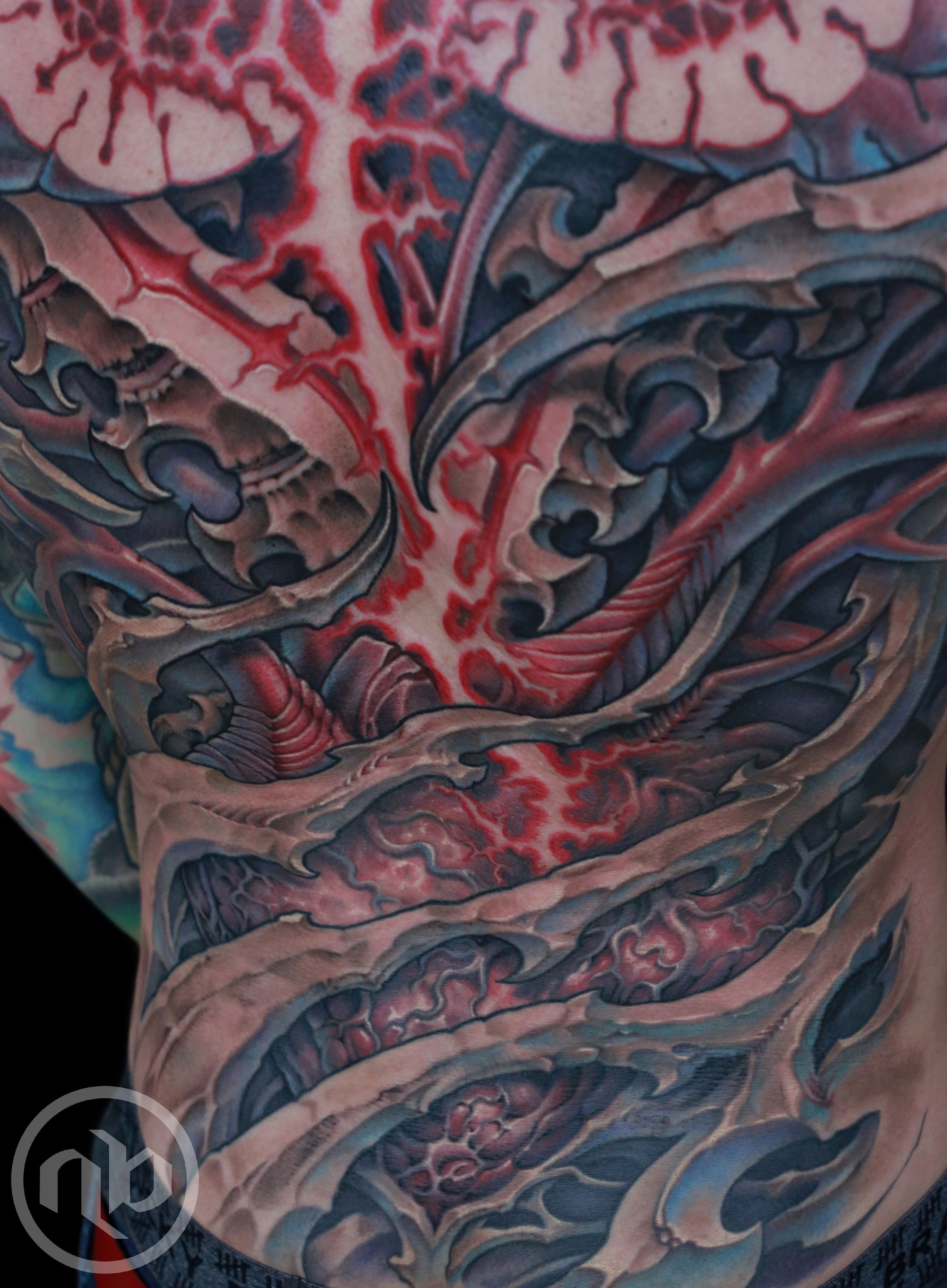 Close detail of a large back tattoo with layered bone-like forms, human heart, and lightning burst.