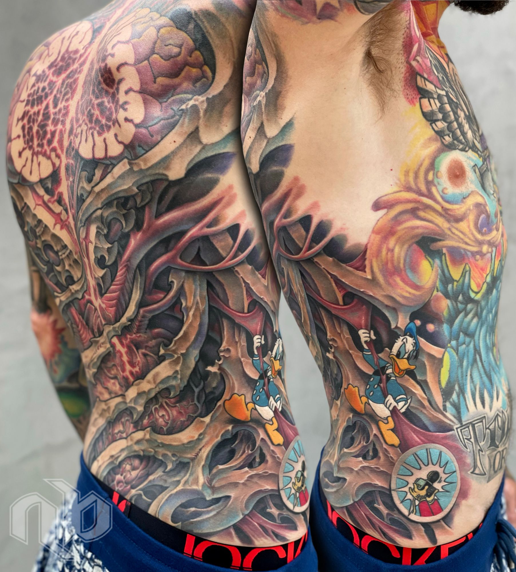 Two close angled views show a large multicolored torso tattoo combining a brain, skeletal organic forms, and cartoon of Donald duck.