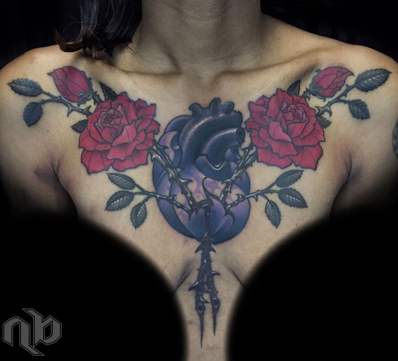 Close view of a chest tattoo featuring a purple anatomical heart centered between red roses, buds, dark leaves, and thorny stems.