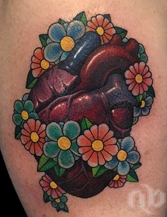 Small arm tattoo of a dark red anatomical heart surrounded by blue, coral, and yellow flowers with green leaves.