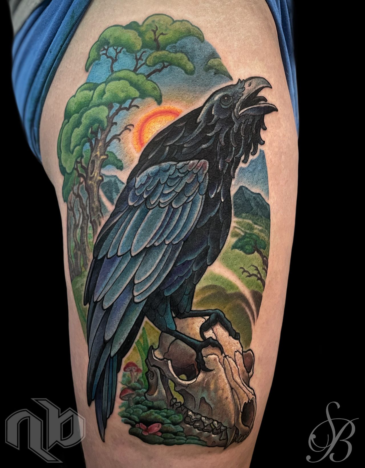 Close view of a colorful leg tattoo showing a black raven above an animal skull, framed by trees, mountains, and sunset.